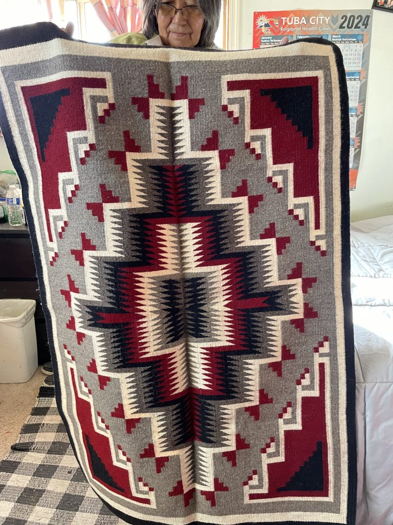 A beautiful hand-woven rug being held up by its creater